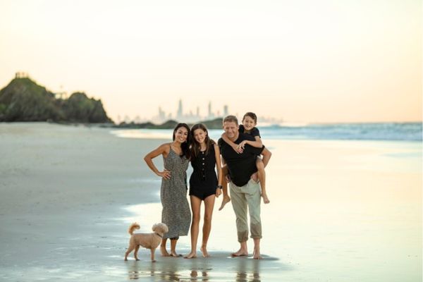 4人の家族と1匹の犬が浜辺に立っている